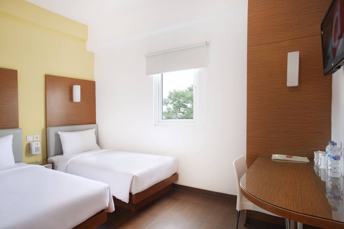 Ein Hotelzimmer mit zwei Betten, einem kleinen Tisch, einem Stuhl, einem Fenster mit Blick und einem an der Wand befestigten Fernseher.