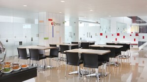A modern dining area with tables and chairs, a buffet with various dishes, and a glass wall with a logo. - Amaris Hotel Malang (Malang)