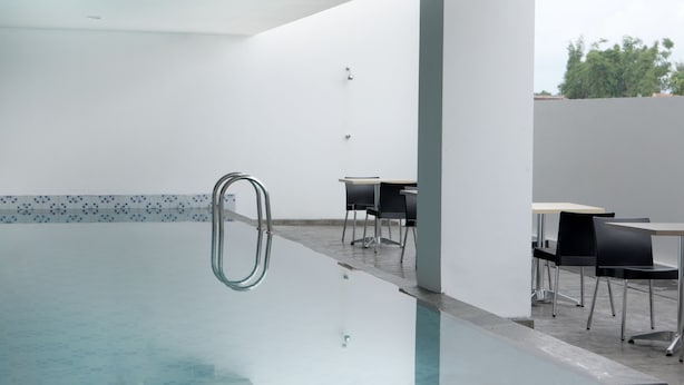 A modern indoor swimming pool with a clear water surface, surrounded by minimalist black chairs and tables, and a simple white wall with a patterned border. - Amaris Hotel Malang (Malang)
