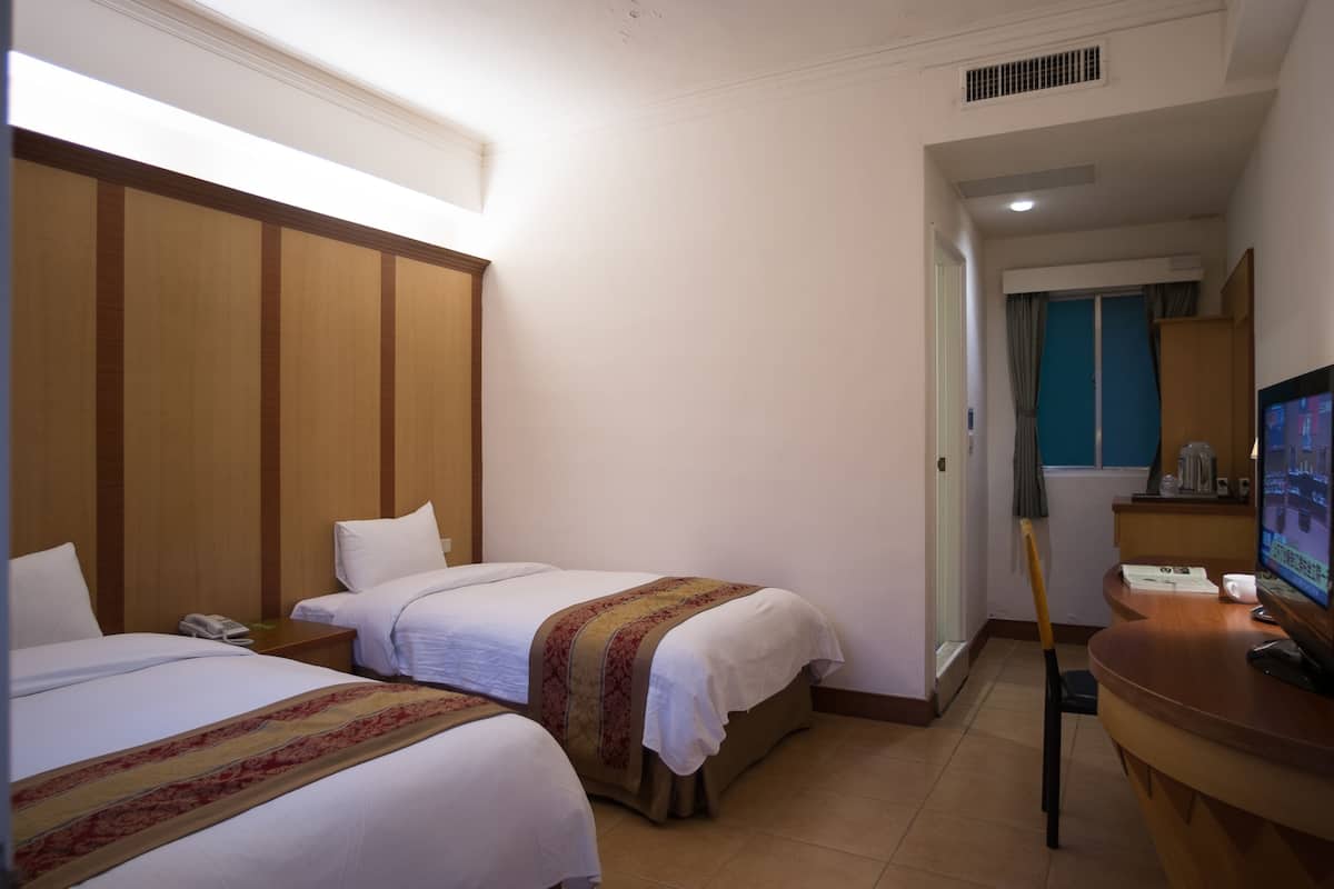 A hotel room with two beds, a desk, a television, and a window with curtains.