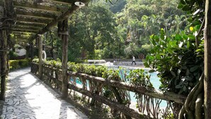 A covered walkway with a tiled floor, a wooden fence, and a pool area surrounded by lush greenery. - Rainbow Resort (Taimali)