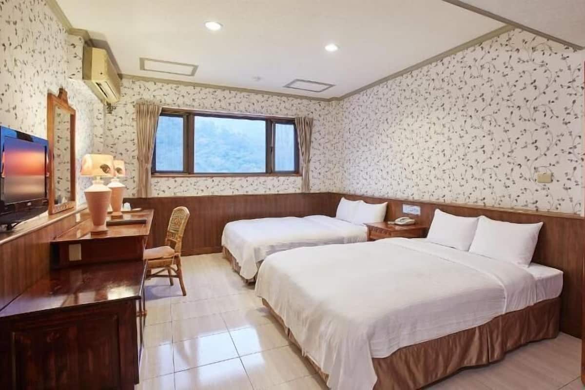 A hotel room with two beds, a desk with a lamp, a TV, and a window.