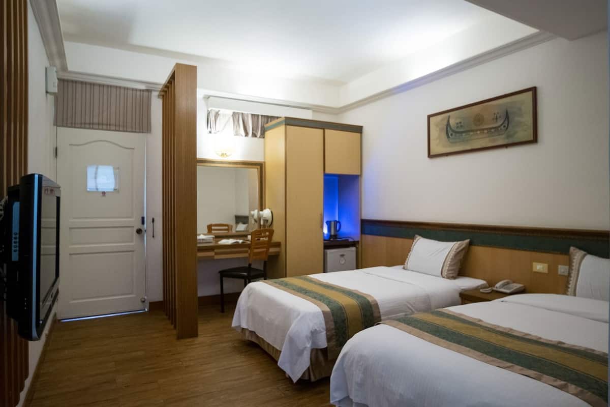 A hotel room with two beds, a desk, a mirror, a wardrobe, and a television.
