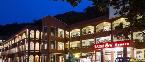A multi-story building with a prominent "Rainbow Resort" sign. There are several vehicles parked in front, including a van and a car.