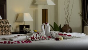 A neatly made bed with rose petals and a towel swan centerpiece, a bedside lamp, and a patterned pillow. - Gowongan Inn Yogyakarta (Yogyakarta)