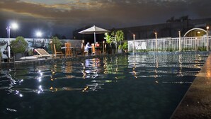 An outdoor swimming pool with a few lounge chairs and umbrellas, surrounded by a white fence and a building in the background. - Gowongan Inn Yogyakarta (Yogyakarta)