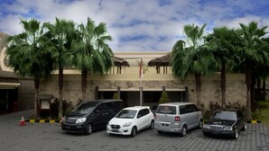 A parking area with four cars, palm trees, and a building with a thatched roof entrance. - Gowongan Inn Yogyakarta (Yogyakarta)