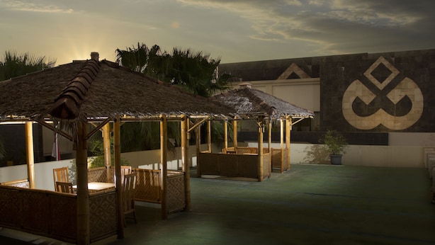 A covered outdoor seating area with bamboo furniture, a thatched roof, and a large wall with a geometric design. - Gowongan Inn Yogyakarta (Yogyakarta)