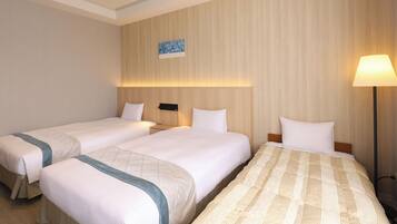 Habitación de hotel con tres camas, una mesita de noche, una lámpara y una obra de arte colgada en la pared.