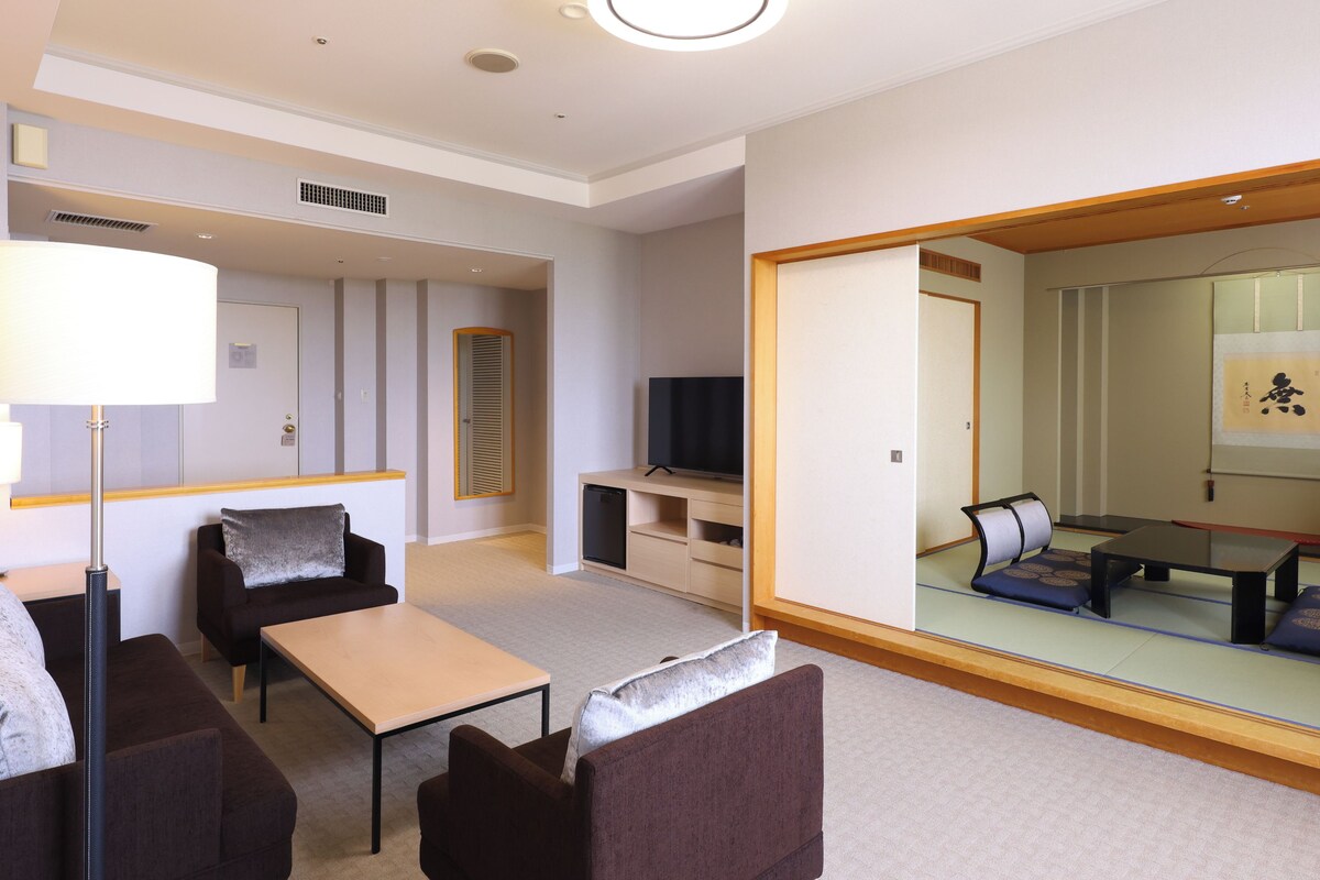 A hotel room with a sofa set, a small table, a TV, and a large mirror.