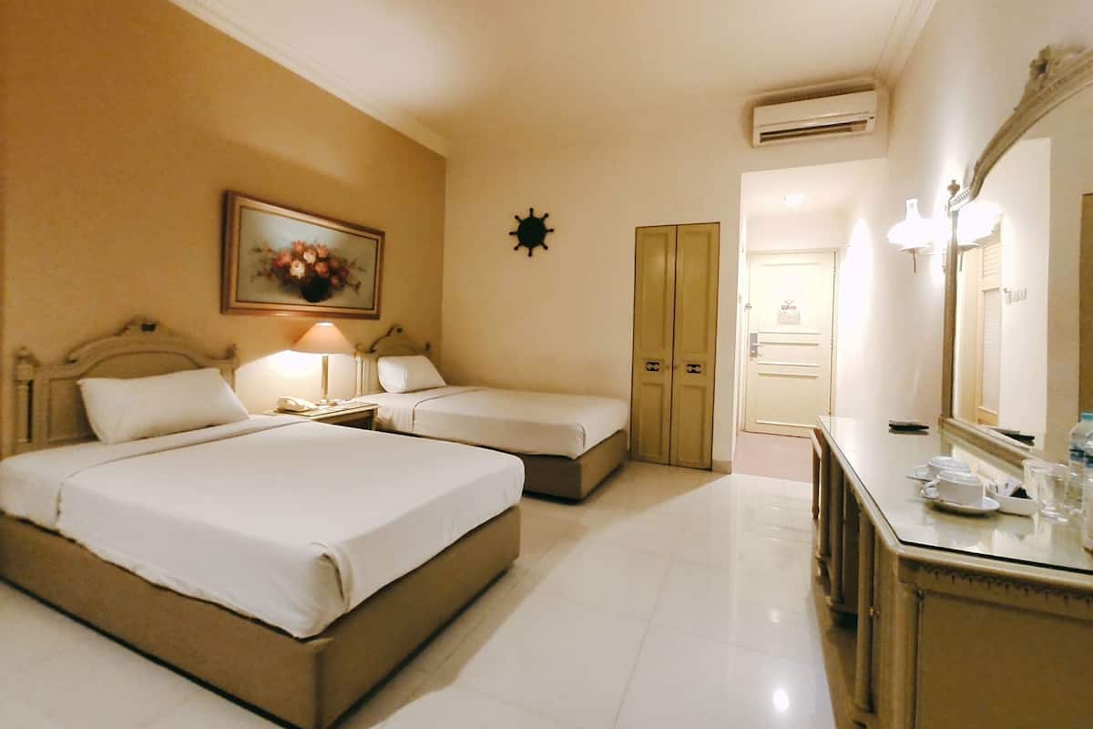 A hotel room with two beds, a desk, a mirror, a wardrobe, and an air conditioning unit.
