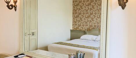 Ein Hotelzimmer mit einem großen Spiegel, einem Bett mit einem gemusterten Kopfteil, einem Marmorschreibtisch mit Wasserkocher, Tassen und einer Fernbedienung.