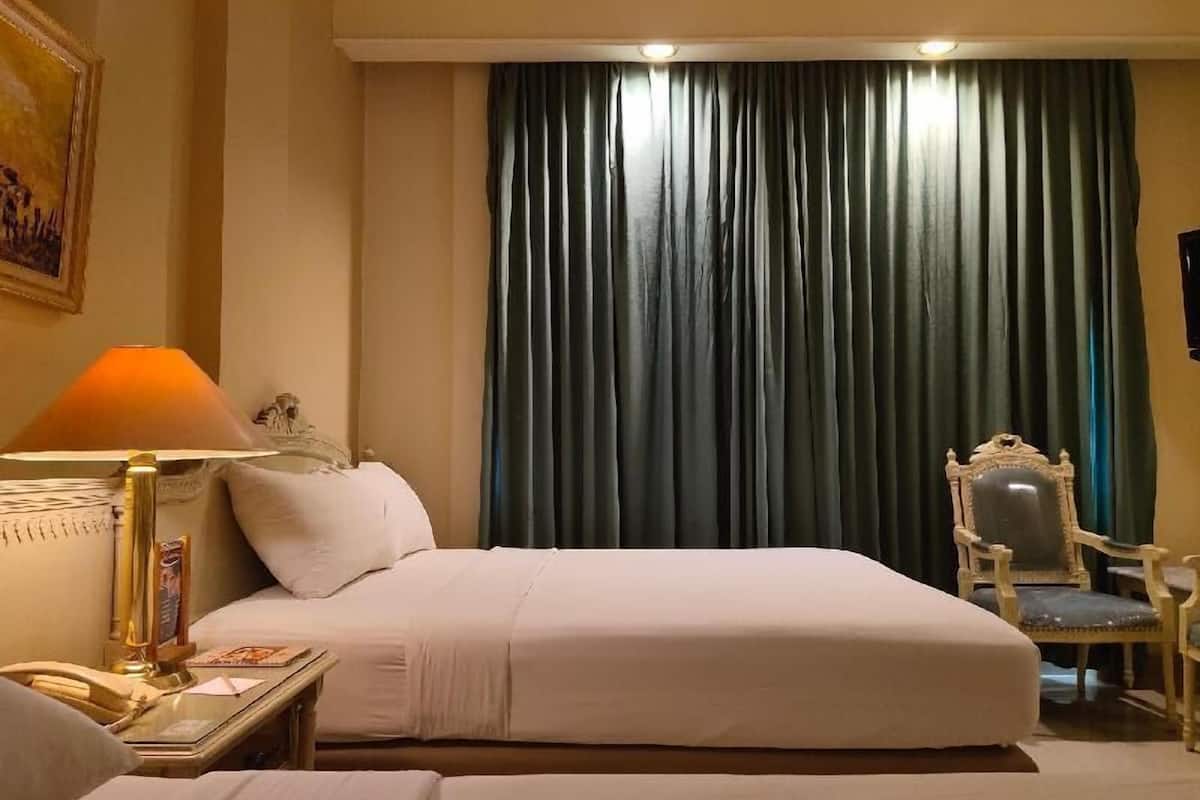 A hotel room with a bed, a chair, a lamp, and a painting on the wall.
