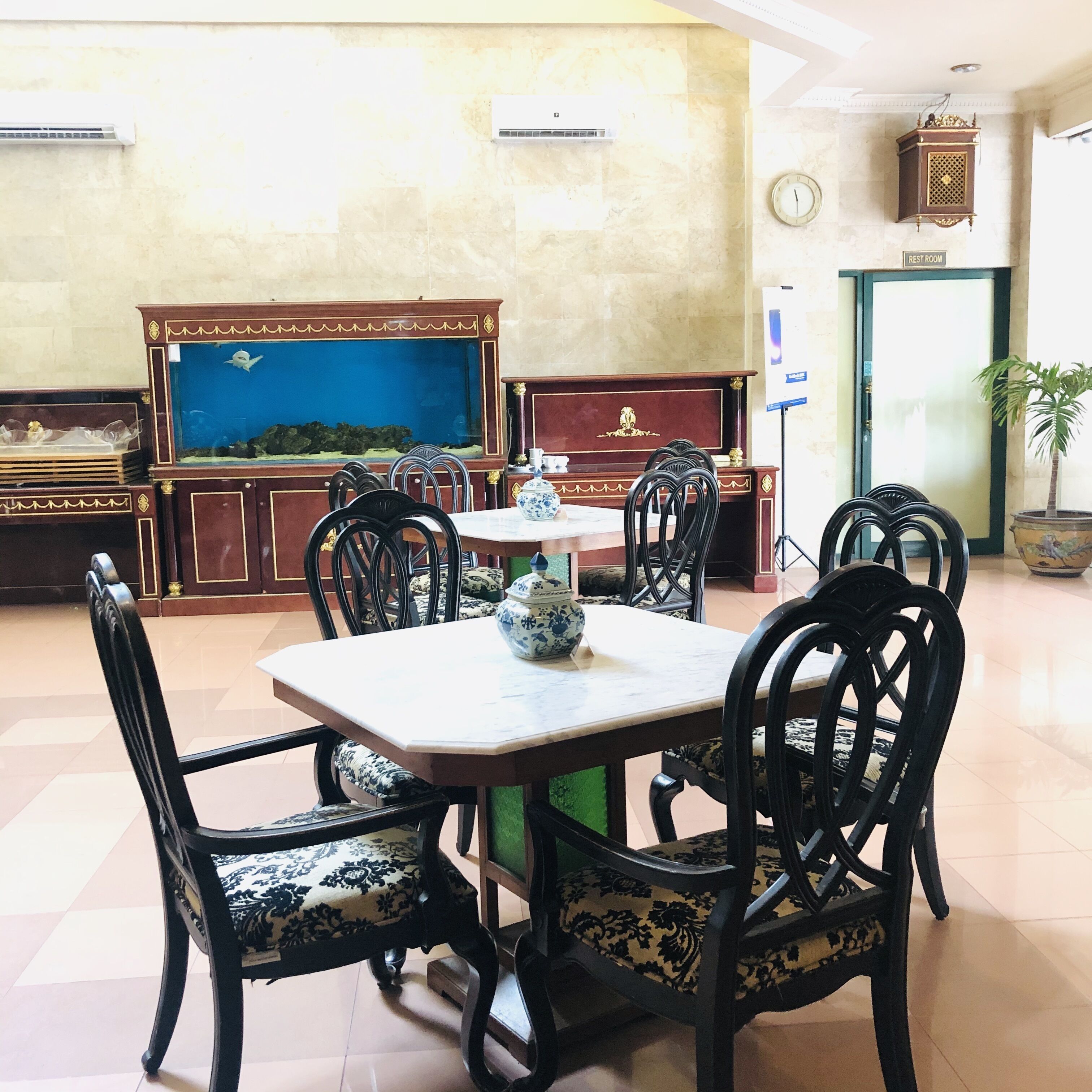 A dining area with a table and chairs, a fish tank, a clock, and a sign indicating a rest room.