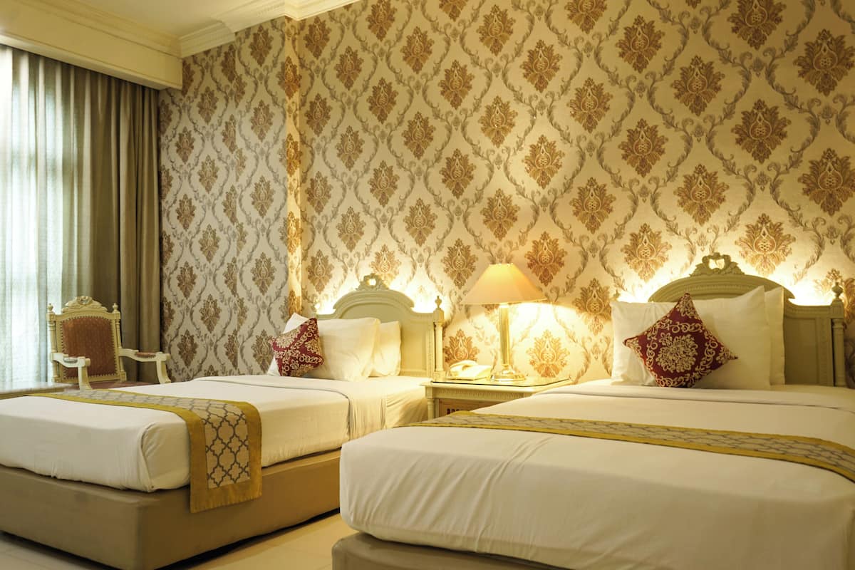 A hotel room with two beds, a nightstand, a lamp, and a chair.