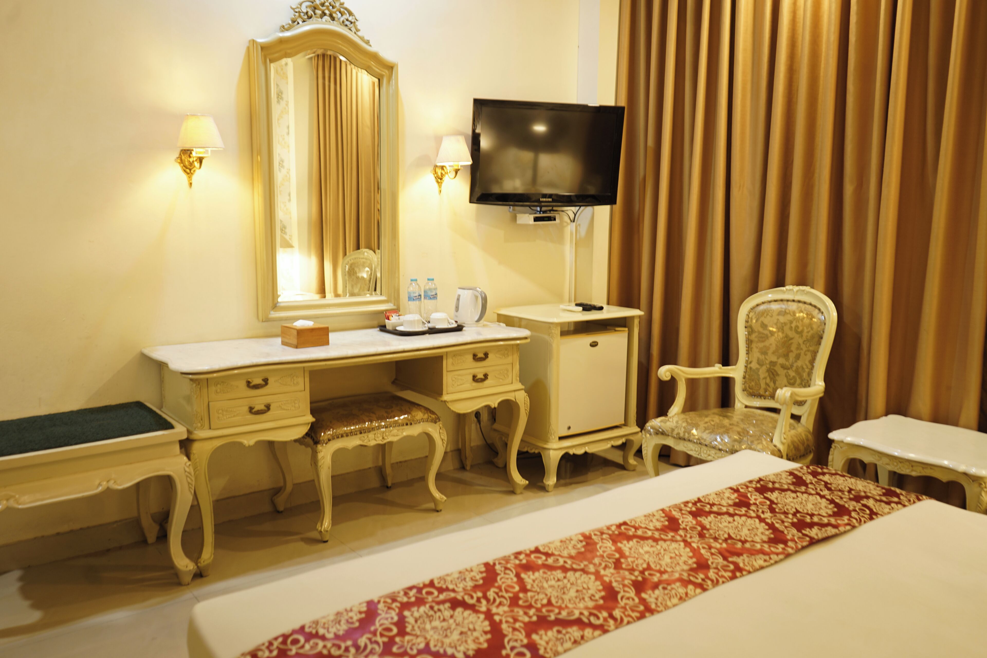 Una habitación de hotel con cama, escritorio con espejo, televisión, silla y una mesita.