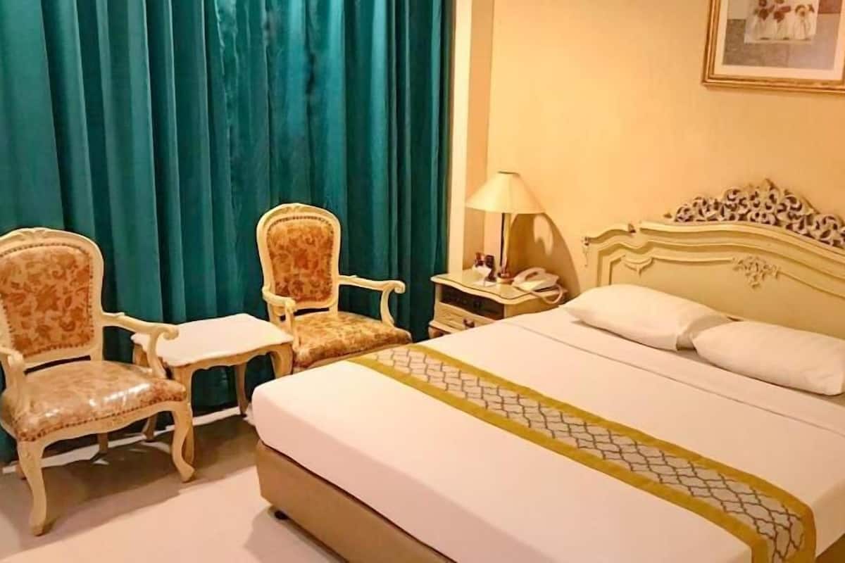 A hotel room with a bed, two chairs, a nightstand, a lamp, and a framed picture on the wall.