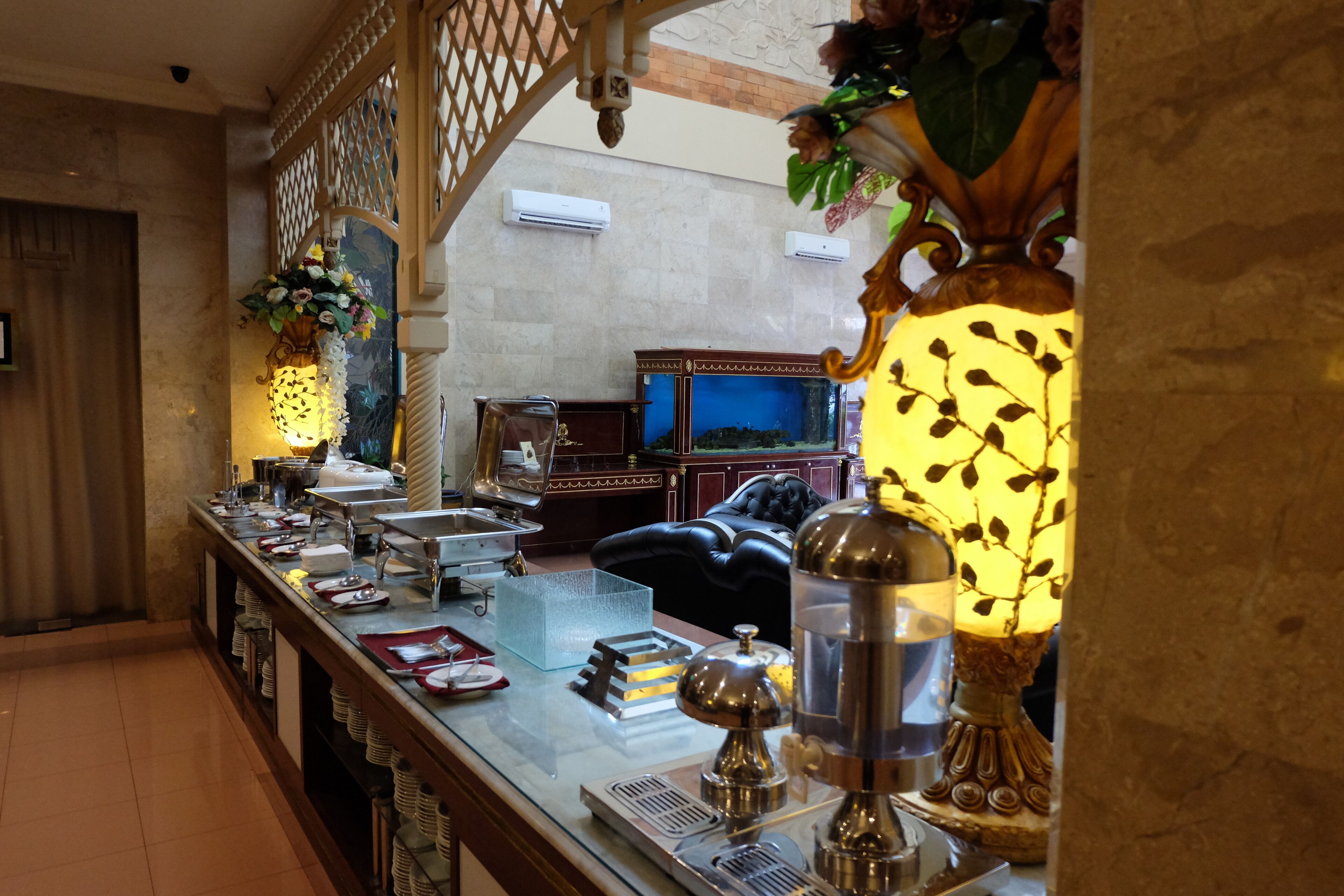 A buffet setup with a variety of dishes, a water dispenser, and decorative elements like flowers and a lamp.