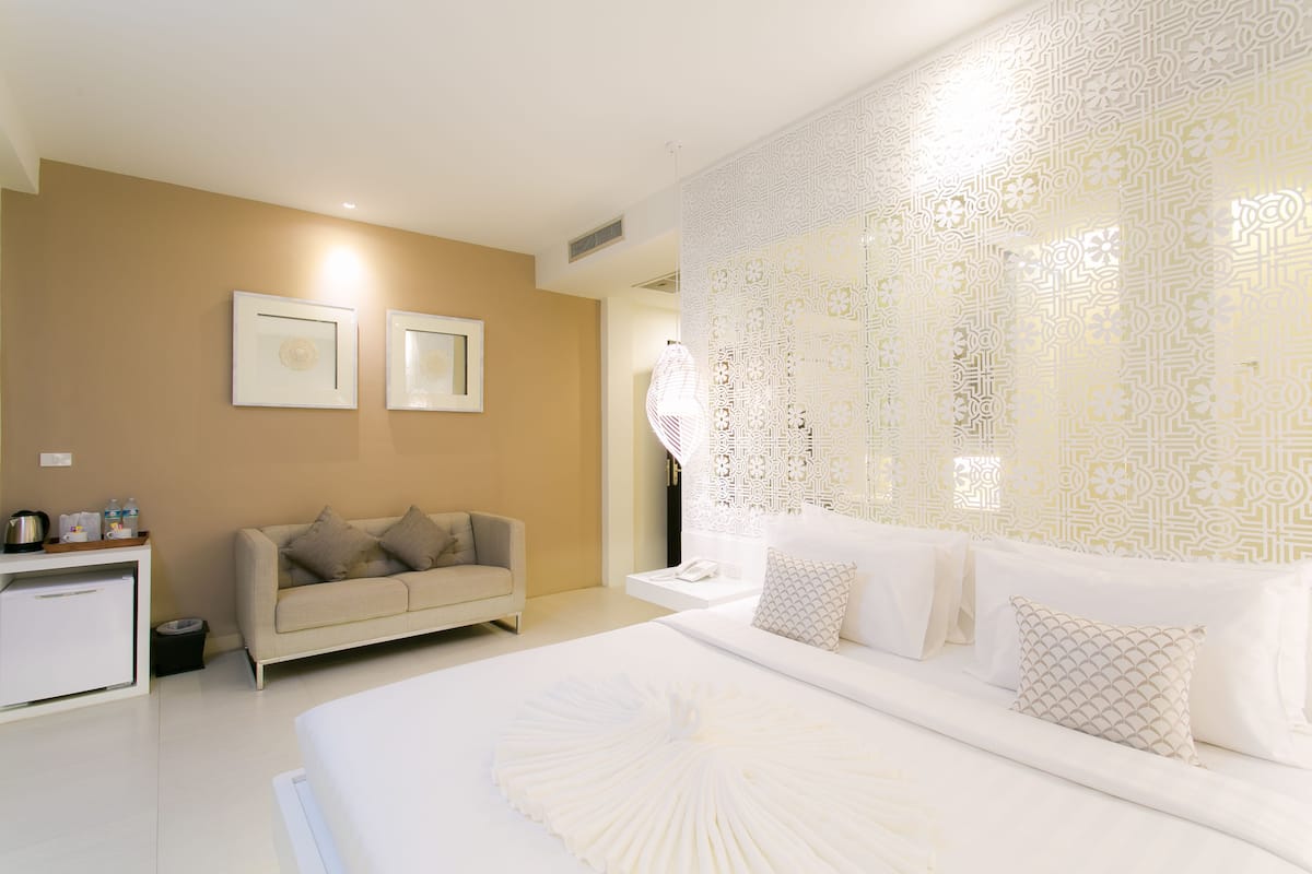 A modern hotel room with a large bed, a sofa, and a small desk.