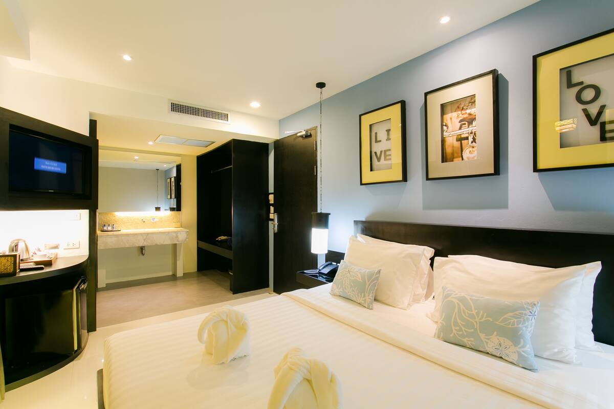 A hotel room with a bed, a desk, a TV, and a bathroom visible through an open door.