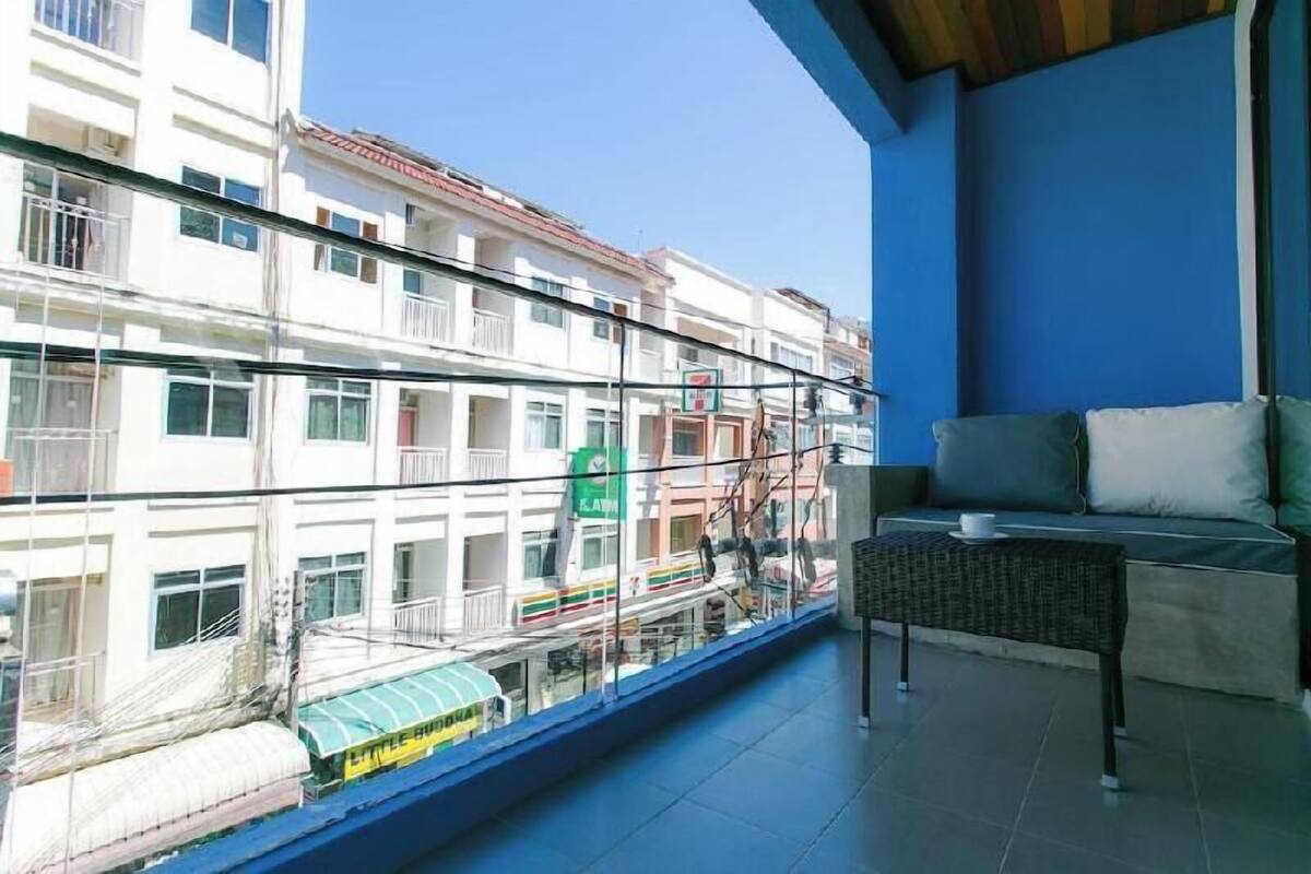 A balcony with a view of a multi-story building, a sofa, and a small table.