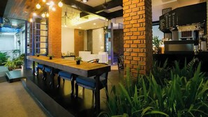 A modern indoor dining area with a long wooden table, multiple chairs, hanging pendant lights, and brick accents. - The House Patong (Patong)