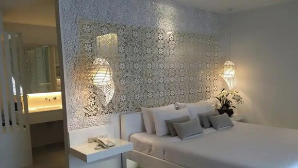 A modern bedroom with a large bed, a bedside table with a lamp, and a decorative wall panel. - The House Patong (Patong)