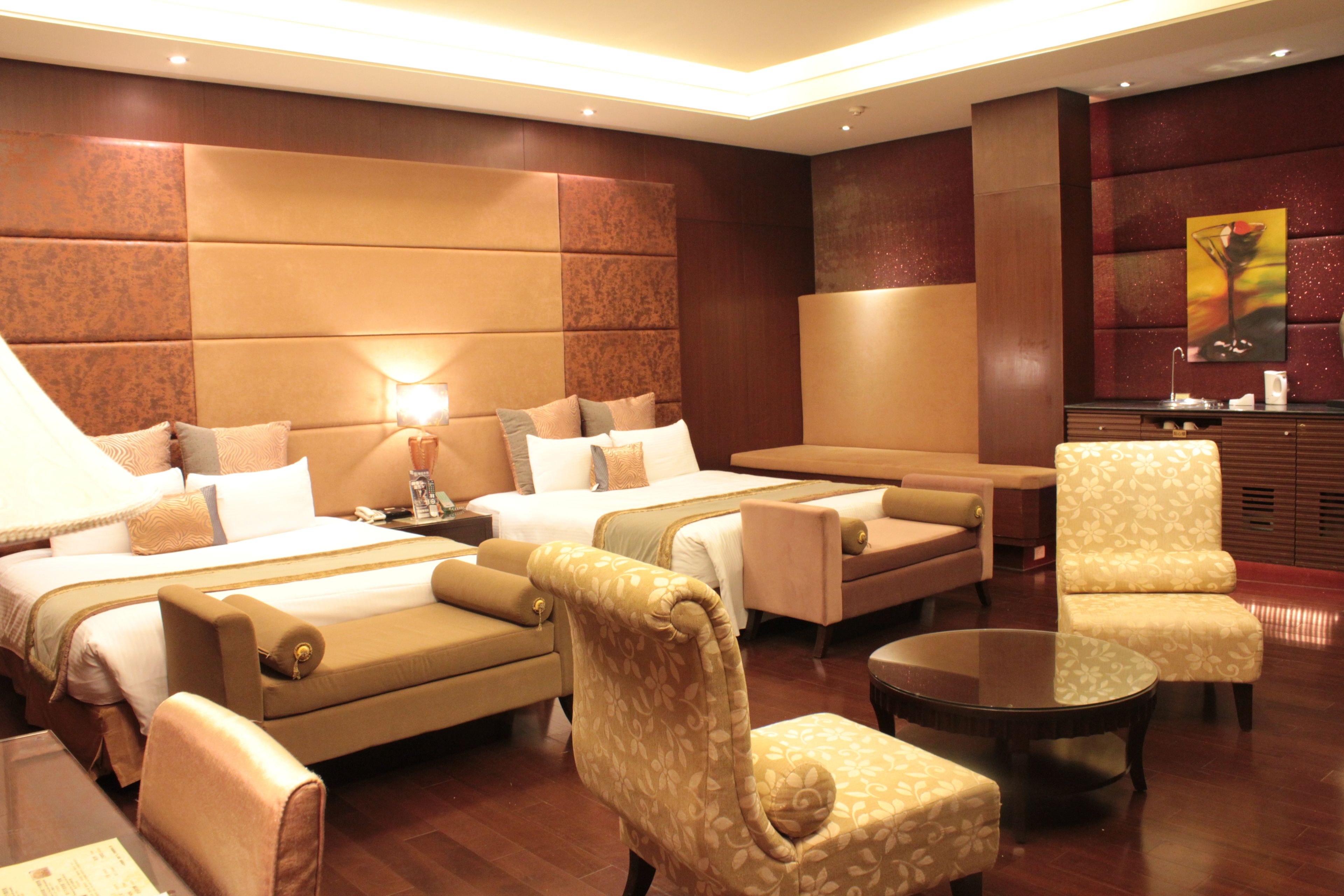 A hotel room with two beds, a sofa, a chair, a small table, and a large mirror.
