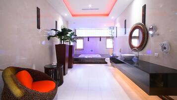 A modern bathroom with a large mirror, a bathtub, and a seating area with a red cushion.
