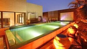 Un área de piscina moderna al aire libre con cerramiento de cristal, cubierta de madera y macetas decorativas.
