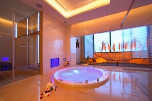 A modern spa room with a large circular hot tub, a glass shower enclosure, and a view of pampas grass through the windows. - Amain Boutique Motel Tucheng (New Taipei City)