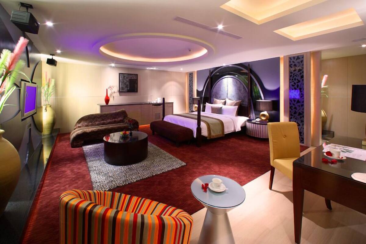 Quarto de hotel moderno com uma cama grande, um sofá, uma mesa de centro e uma escrivaninha.