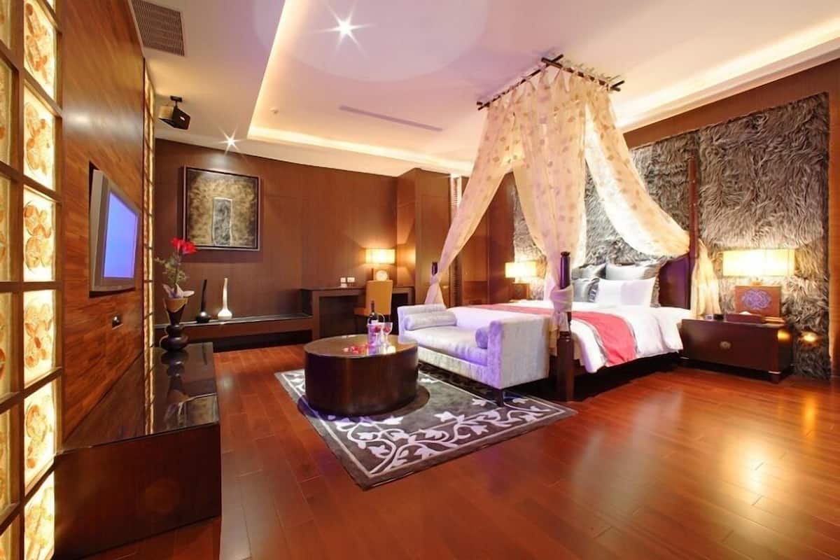 Quarto de hotel com cama, mesas de cabeceira, televisão, parede decorativa e uma janela grande.