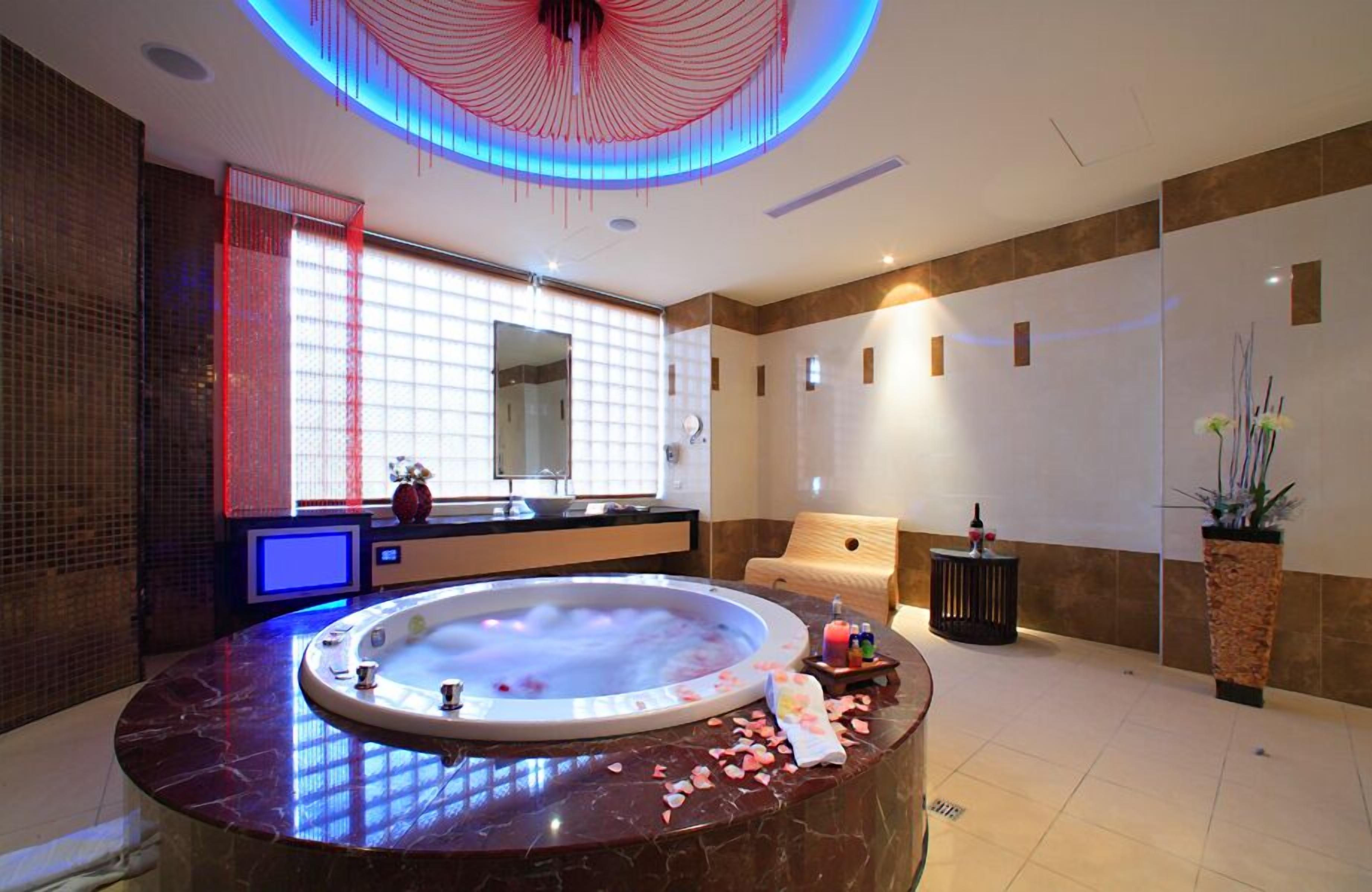 Een moderne spa ruimte met een groot rond bubbelbad, een grote spiegel en een houten massagetafel.