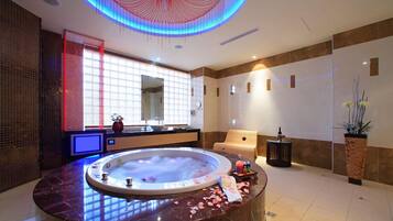 Een moderne spa ruimte met een groot rond bubbelbad, een grote spiegel en een houten massagetafel.