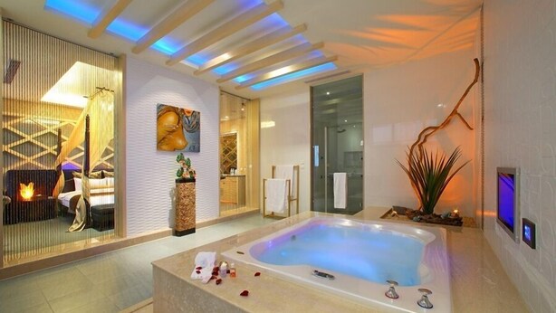 Un moderno cuarto de spa con una bañera grande, una zona de estar con chimenea y un televisor montado en la pared.