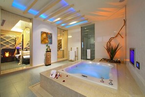 Une salle de spa moderne dotée d’une grande baignoire, d’un coin salon avec un foyer et d’un téléviseur fixé au mur.