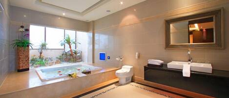 A modern bathroom with a bathtub, toilet, and sink, featuring a large mirror and potted plants.