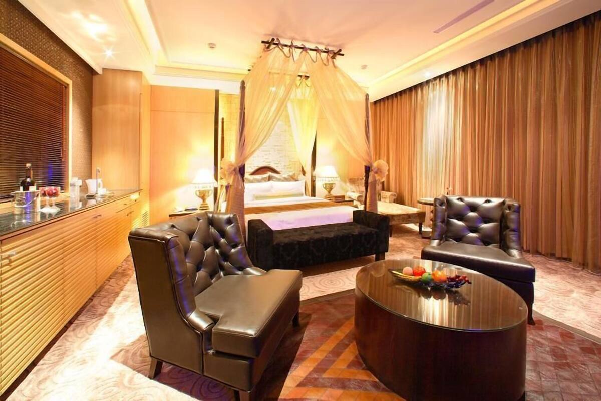 Um quarto de hotel luxuoso com cama de dossel, assentos de couro, uma mesa de centro redonda e um minibar.