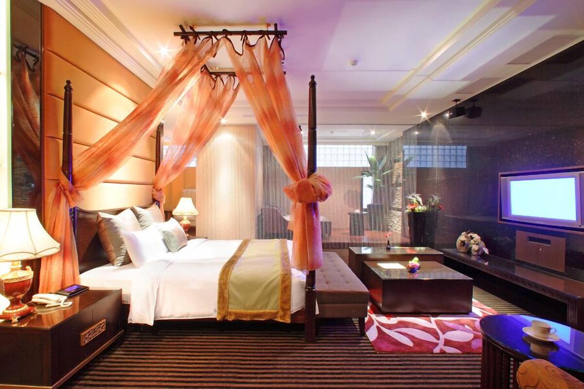 Quarto de hotel com cama de dossel, televisão de tela plana, sofá, mesa de centro e uma pequena mesa com uma xícara.