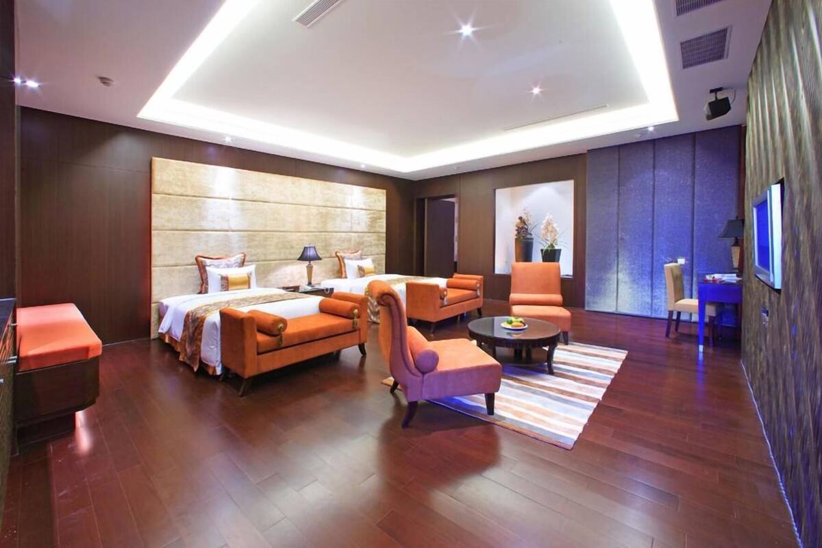 Quarto de hotel moderno com uma cama grande, duas poltronas laranjas, uma mesa pequena e uma TV.
