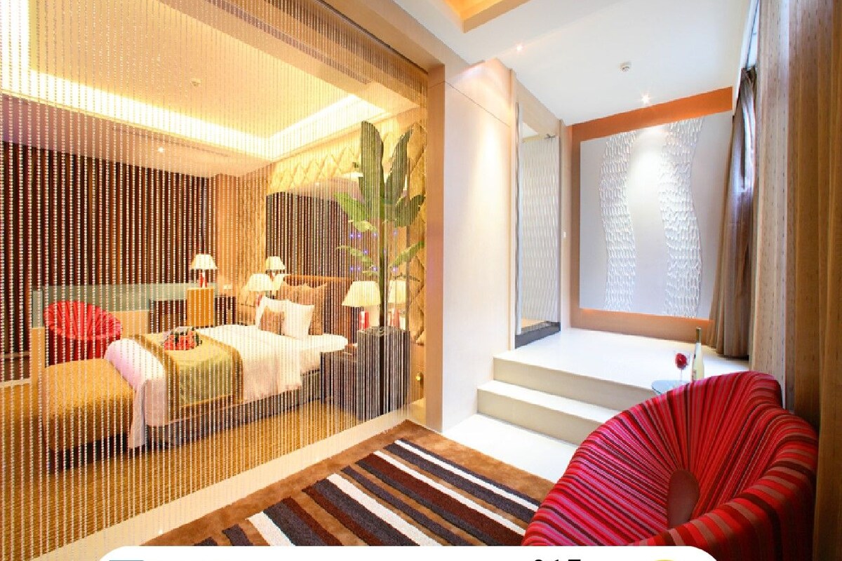A modern hotel room with a bed, bedside tables, and a red chair. There is a staircase leading to an upper level.