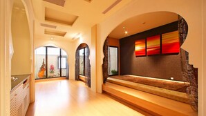 Un pasillo amplio con piso de madera, una zona de estar con un banco acolchado y una pared decorada con pinturas abstractas.