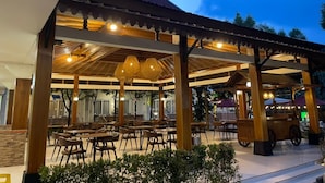 An outdoor dining area with wooden tables and chairs, a covered seating area, and a food cart. - Hotel Indah Palace Tawangmangu (Tawangmangu)