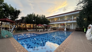 A swimming pool with tiled patterns, surrounded by lounge chairs and umbrellas, with a building in the background. - Hotel Indah Palace Tawangmangu (Tawangmangu)