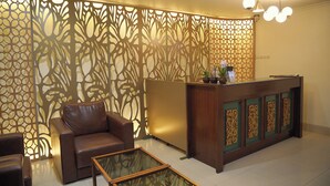 A reception area with a brown leather sofa, a glass-top coffee table, a wooden reception desk with decorative panels, and a modern chandelier. - Hotel Indah Palace Tawangmangu (Tawangmangu)