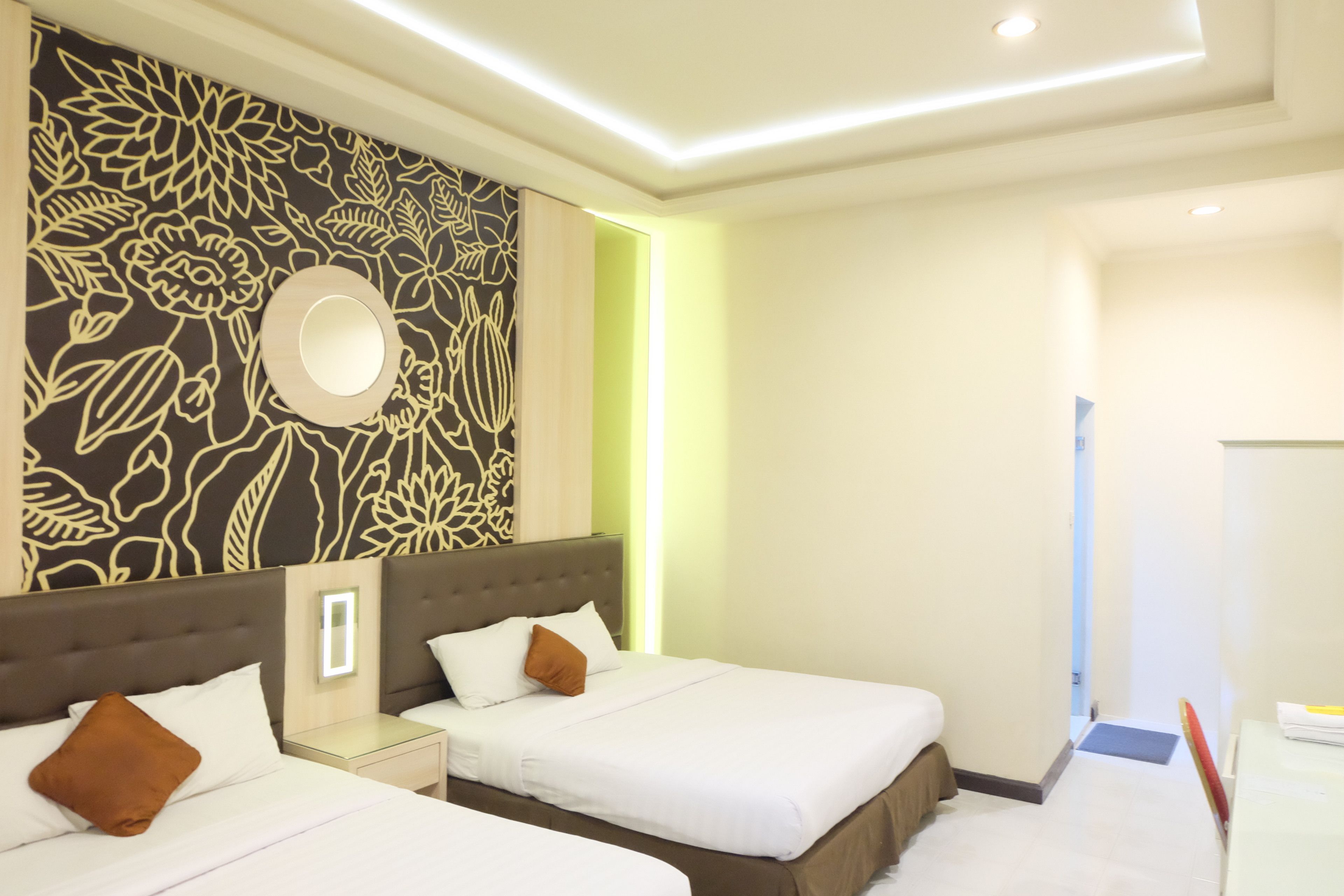 Een hotelkamer met twee bedden, een decoratieve wand met bloemmotieven, een ronde spiegel en een nachtkastje met een lamp.
