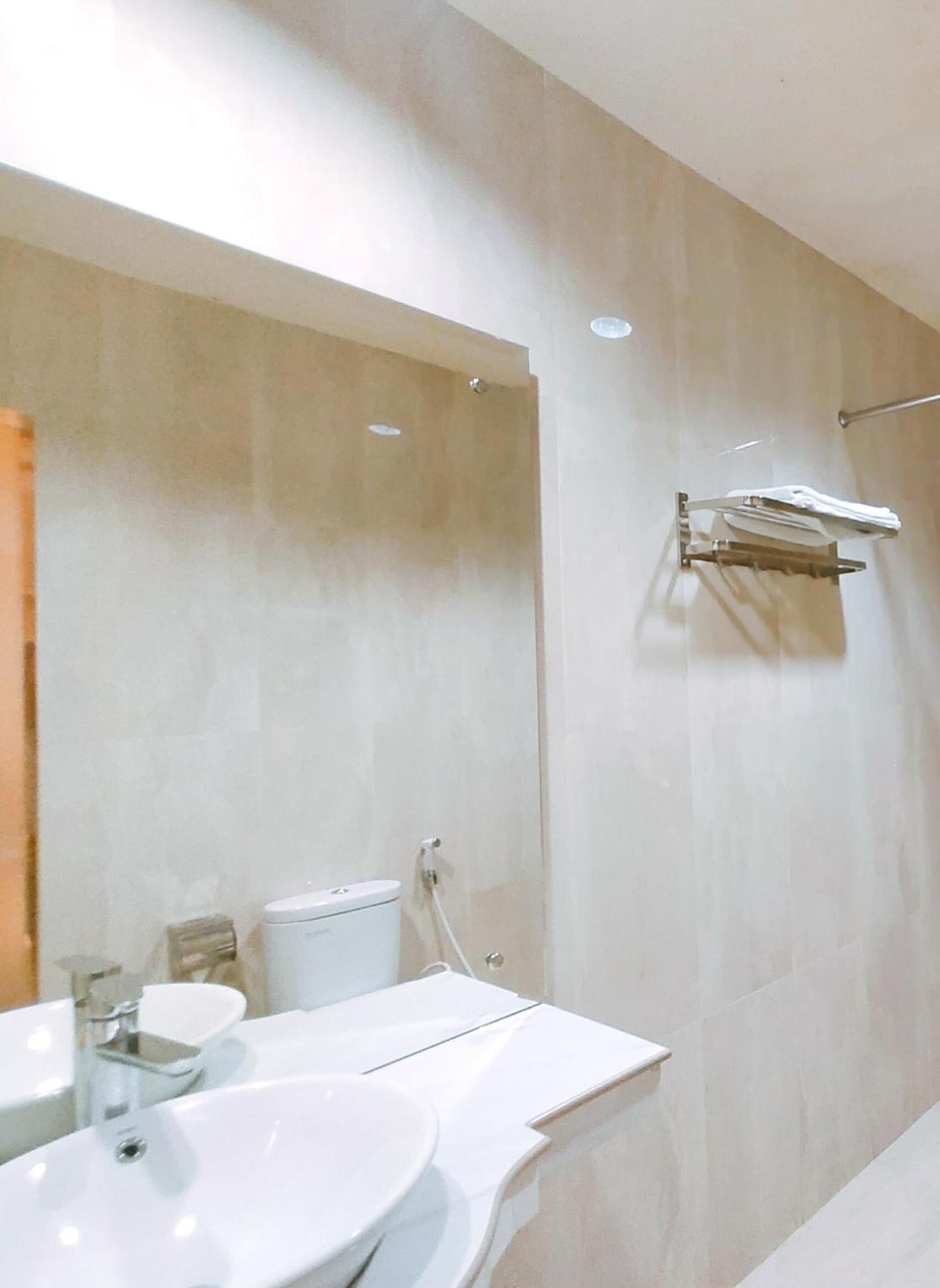 A modern bathroom with a large mirror, a white sink, and a toilet. There is a towel rack on the wall.