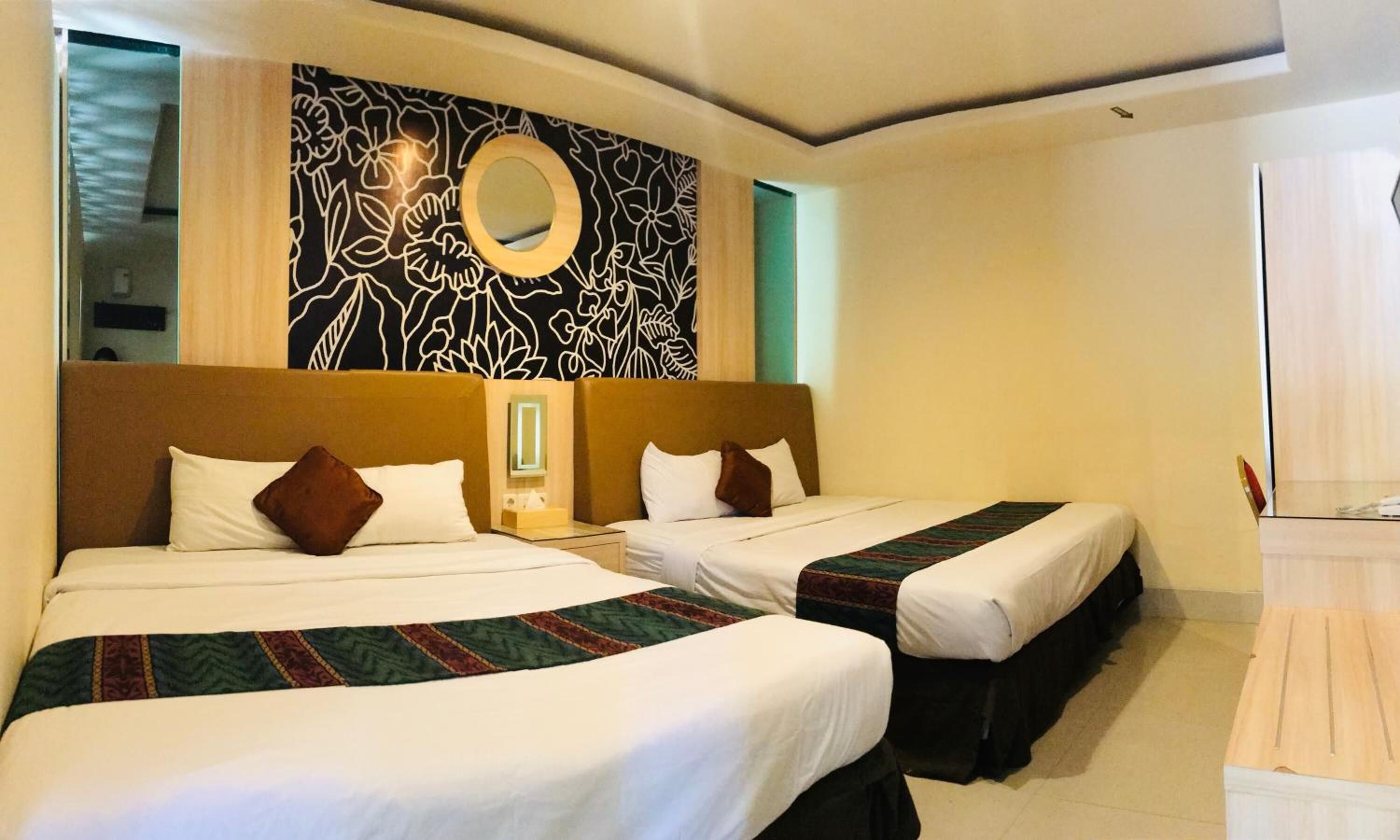 A hotel room with two beds, a mirror, and a wall with a floral pattern.