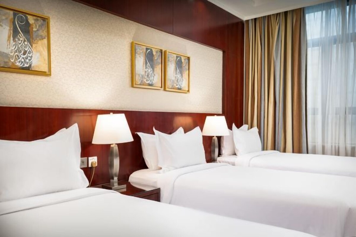 Habitación de hotel con tres camas, un cabecero de madera y dos lámparas fijadas a la pared.